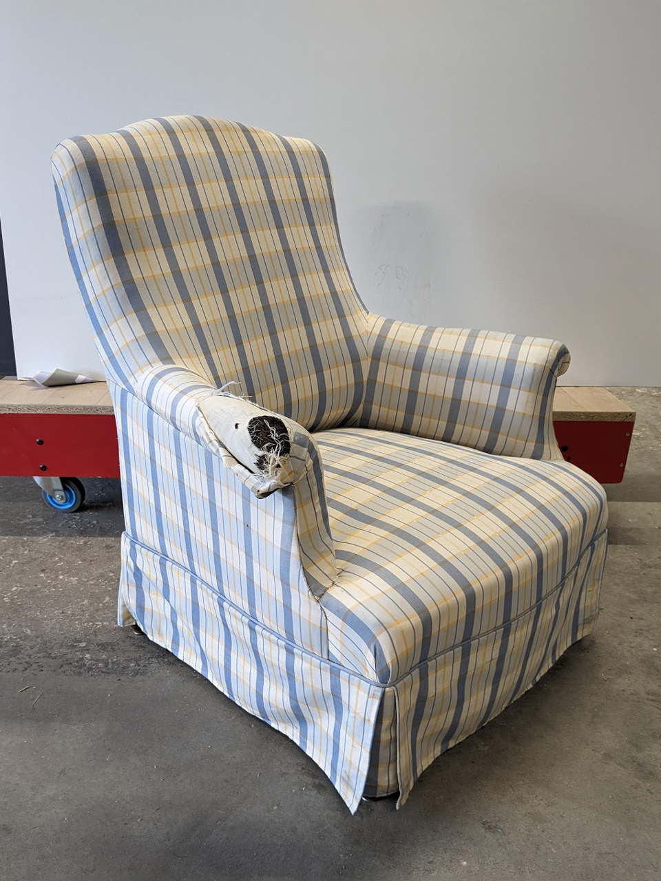 Le fauteuil a un tissu à carreaux jaune et bleu. Il y a une jupette autour des pieds. Le tissu est déchiré par endroits!